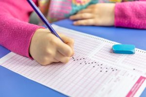 image of child's hand holding pencil filling out standardized exam bubbles